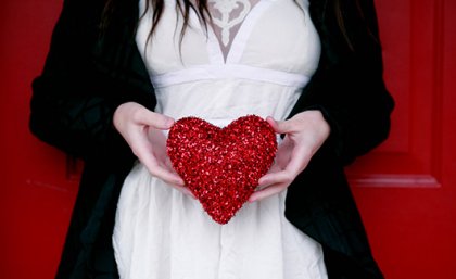 Woman holding a red heart over her stomach.